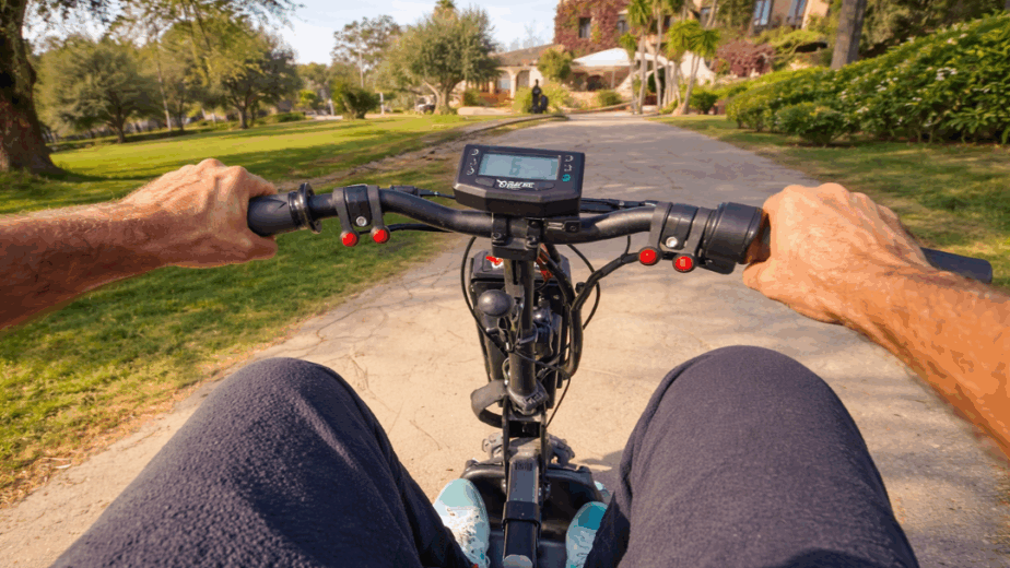 Vista en primera persona conduciendo un dispositivo de movilidad Batec Mobility por un camino, con el manillar y la pantalla al frente.